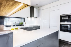 Minimalistická linka v bielej a šedej farbe s kuchynskou stenou až po strop. Pracovnú plochu osvetľuje horizontálne okno