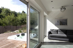 V lete je hlavná obytná miestnosť prepojená s terasou. Vďaka posuvným veľkoformátovým oknám tvorí nedeliteľný celok. Mólo sa zapustenou vírivkou predlžuje terasu do vnútra záhrady. Sibírsky smrekovec fasády farebne ladí s exotickou dlážkovou drevinou massaranduba použitou na vonkajšie povrchy