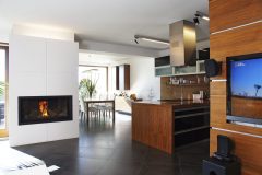 Medzi kuchynskou časťou a sedením je umiestnený atypický kozub s integrovaným osvetlením. Biele obkladové dosky sa krásne odrážajú od antracitovej veľkoformátovej keramickej dlažby