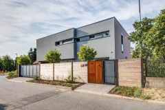 Sivé omietky a rámy okien sú nadčasové a postupne splynú so zeleňou. Plot i vstup na pozemok je vyrobený z dreva a perforovaného oceľového plechu, architektonicky ladia s domom